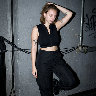 Rave Zip Top schwarz, Model lehnt an Wand, Techno Club Atmosphäre