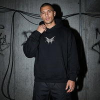 Schwarzer Tribal Techno Vibes Oversize Hoodie, Vorderansicht am Model vor Betonwand #farbe_schwarz
